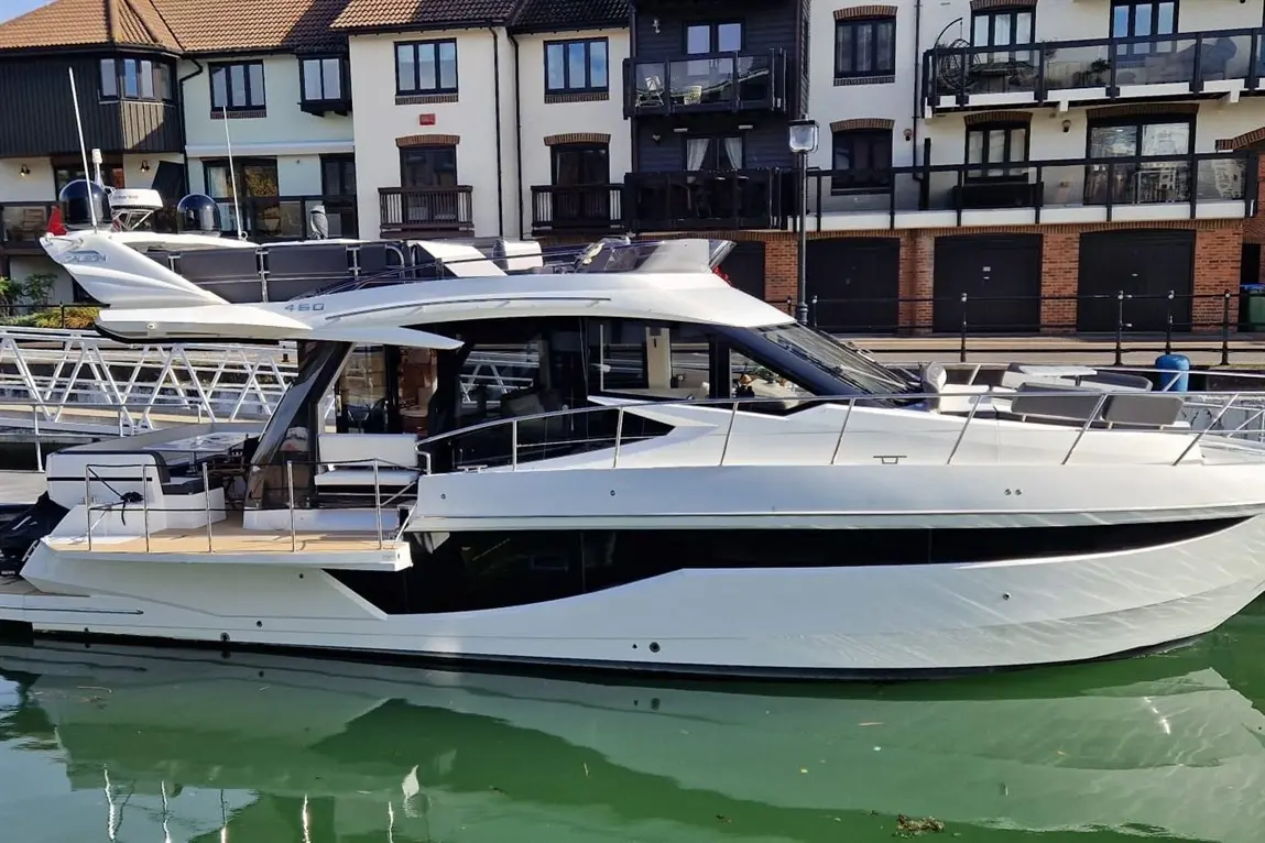 A luxury yacht docked at a marina, with modern design, glass windows, and reflection in the green water.